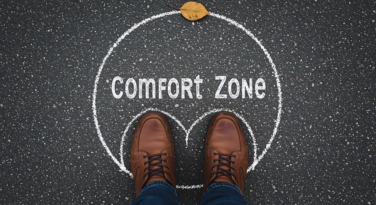 A top view of a persons shoes standing on asphalt inside a chalk circle labeled comfort zone This image represents the concept of pushing oneself out of comfortable situations for personal growth and new experiences It signifies breaking boundaries and achieving success