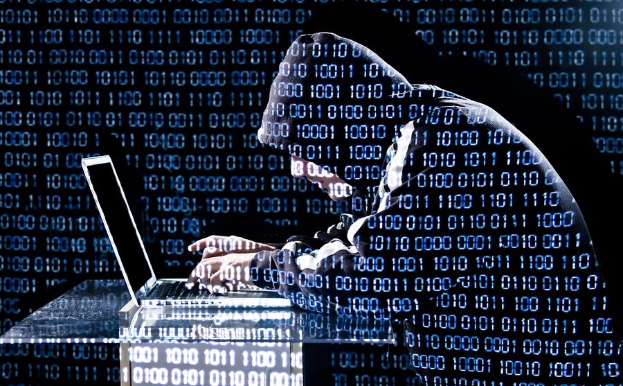 A hooded figure uses a laptop suspiciously.